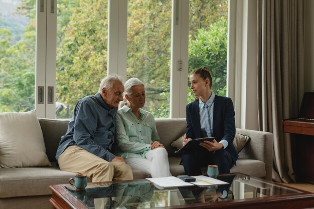 An elderly couple sitting on a couch discussing documents with a professional in a living room.