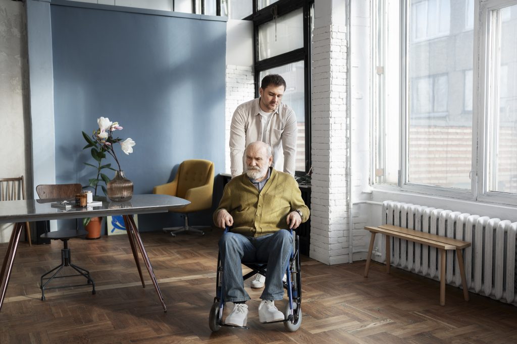 A caregiver pushing an elderly man in a wheelchair inside a modern apartment.